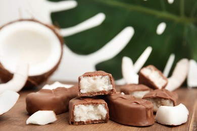 Delicious milk chocolate candy bars with coconut filling on wooden board, closeup. Space for text