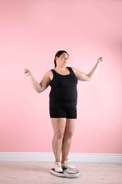 Overweight woman in sportswear using scales near color wall