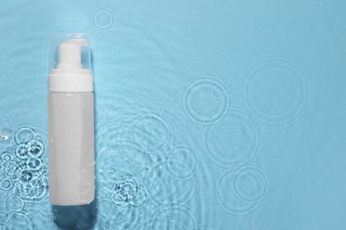 Bottle of face cleansing product in water against light blue background, top view. Space for text