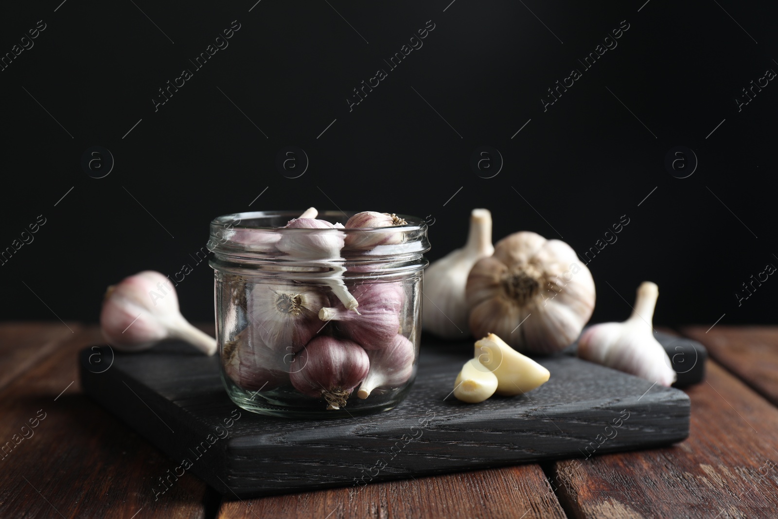 Photo of Many fresh garlic bulbs on wooden table against black background
