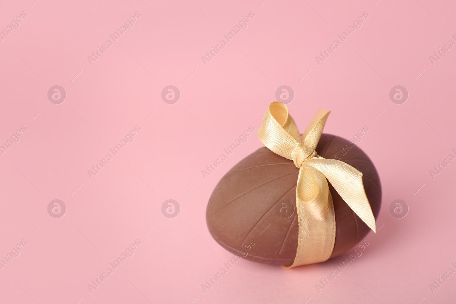 Photo of Sweet chocolate egg with beige bow on pink background. Space for text