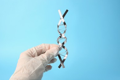 Photo of Scientist with DNA molecular chain model made of metal on light blue background, closeup