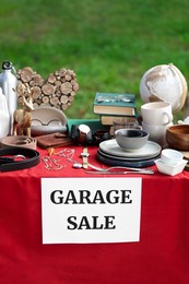 Photo of Paper with sign Garage sale and many different items on red tablecloth in yard
