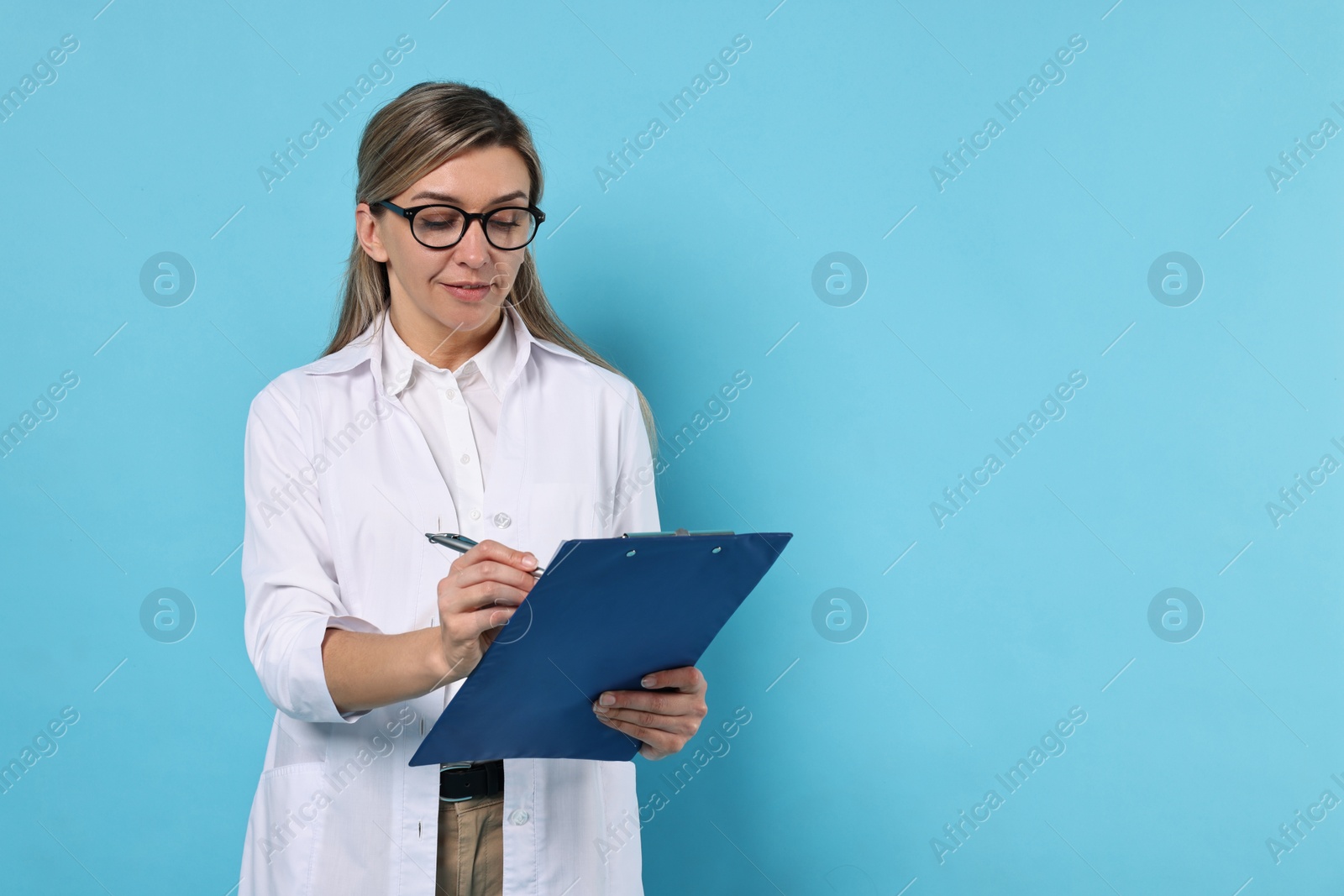 Photo of Portrait of happy doctor with clipboard on light blue background, space for text