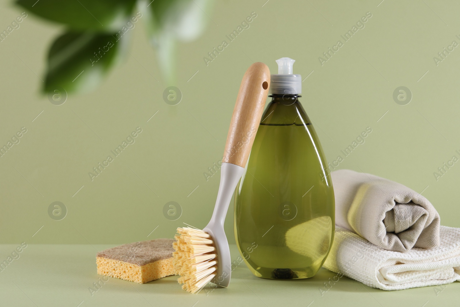 Photo of Bottle of cleaning product, sponge, rags and brush on light green background. Space for text