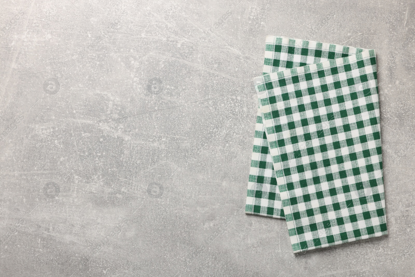 Photo of Green checkered tablecloth on light gray textured table, top view. Space for text
