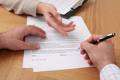 Photo of Businesspeople signing contract at wooden table, closeup of hands