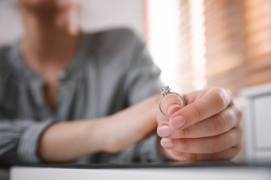 Photo of Woman holding wedding ring at table indoors, space for text. Divorce concept