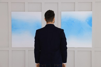 Photo of Young man at exhibition in art gallery, back view