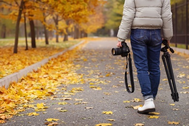 Photo of Photographer with professional camera and tripod outdoors on autumn day, closeup. Space for text