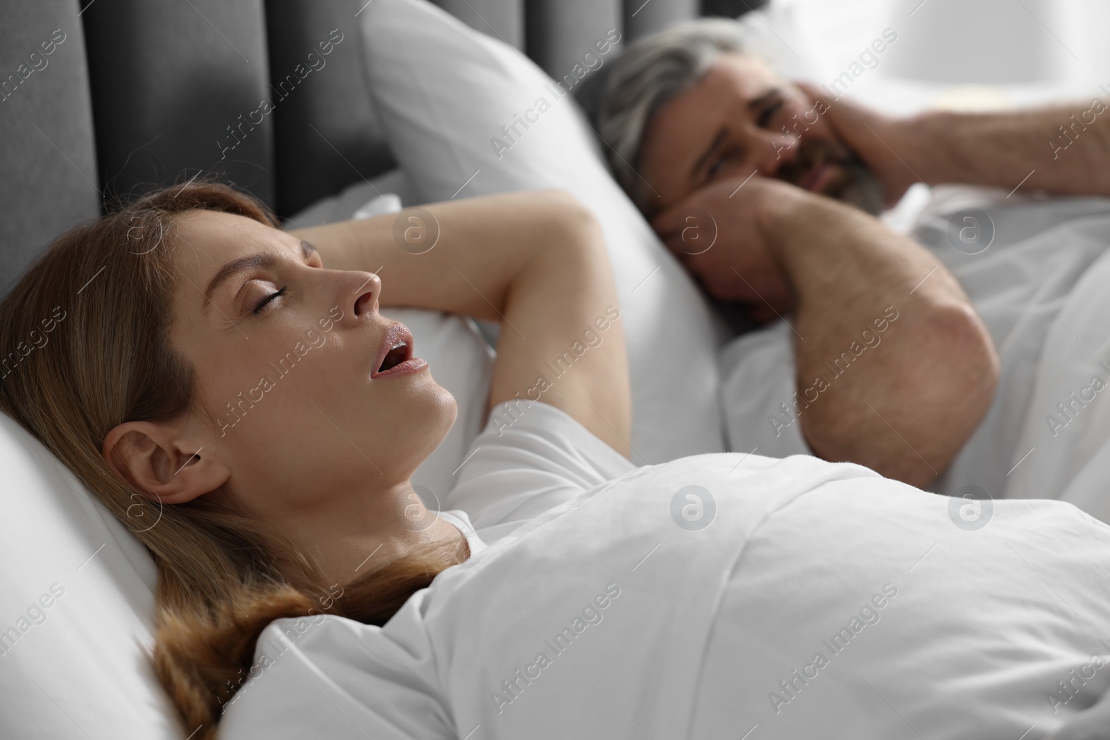 Photo of Irritated man lying near his snoring wife in bed at home