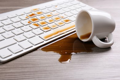 Photo of Cup of coffee spilled over computer keyboard on wooden table