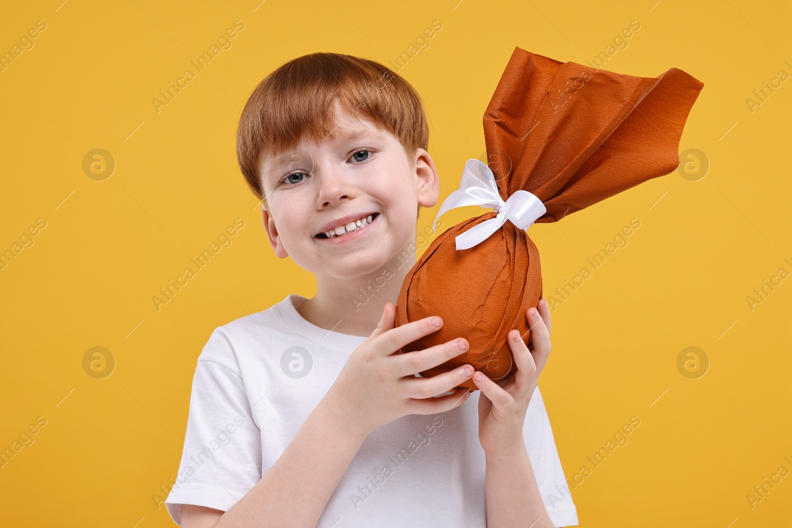 Photo of Easter celebration. Cute little boy with wrapped egg on orange background