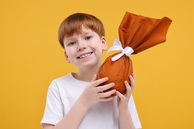 Easter celebration. Cute little boy with wrapped egg on orange background