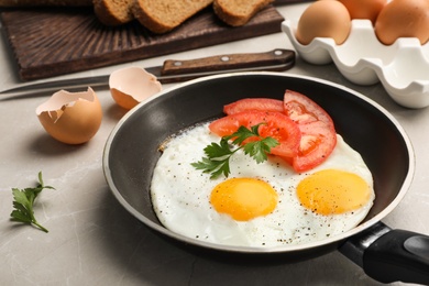 Photo of Pan with fried sunny side up eggs and tomato on table