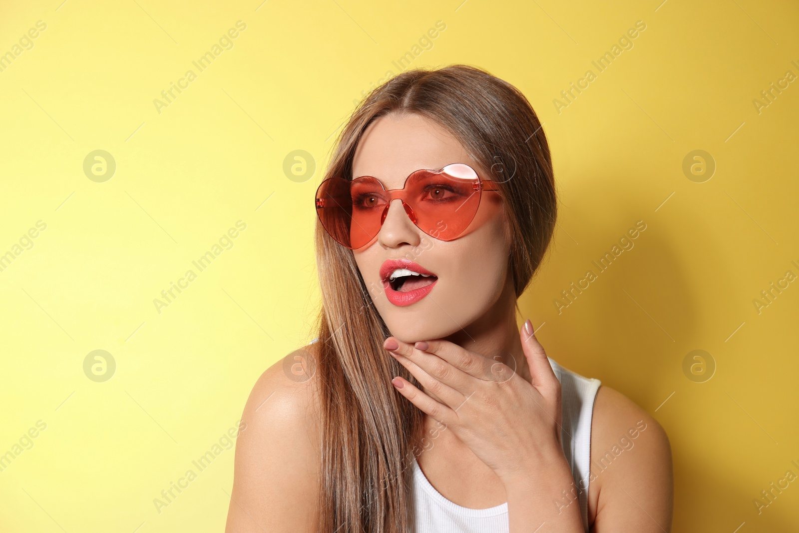 Photo of Young woman wearing stylish heart shaped sunglasses on yellow background