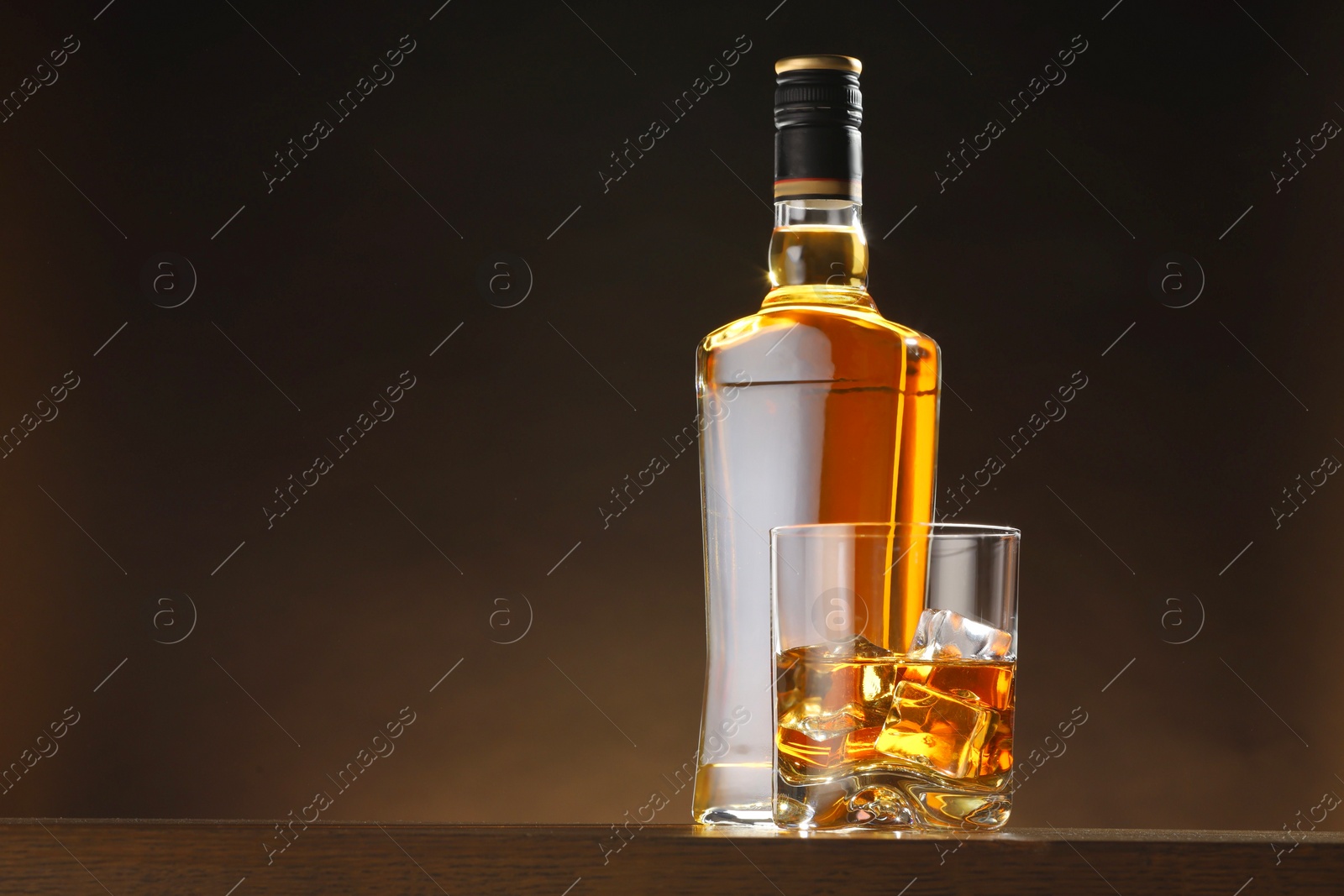 Photo of Whiskey with ice cubes in glass and bottle on table, space for text