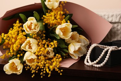 Photo of Bouquet with beautiful spring flowers and necklace on wooden chest of drawers, closeup