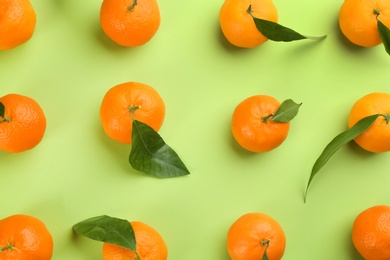 Photo of Fresh tangerines with green leaves on light green background, flat lay