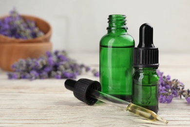 Photo of Bottles with natural lavender oil, dropper and flowers on white wooden table, closeup view. Space for text