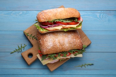 Photo of Delicious sandwiches with fresh vegetables, cheese and arugula on light blue wooden table, flat lay