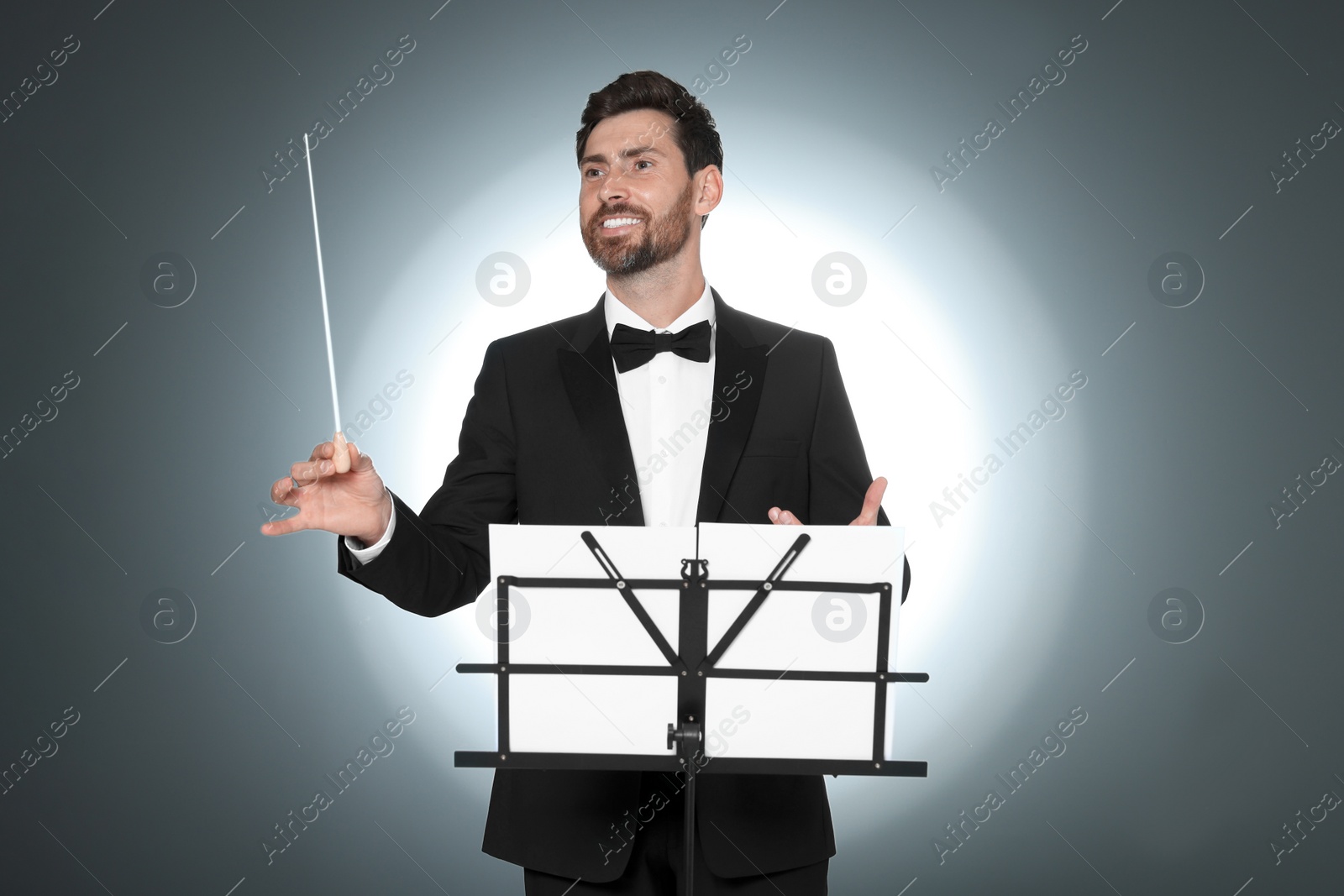 Photo of Happy professional conductor with baton and note stand on grey background