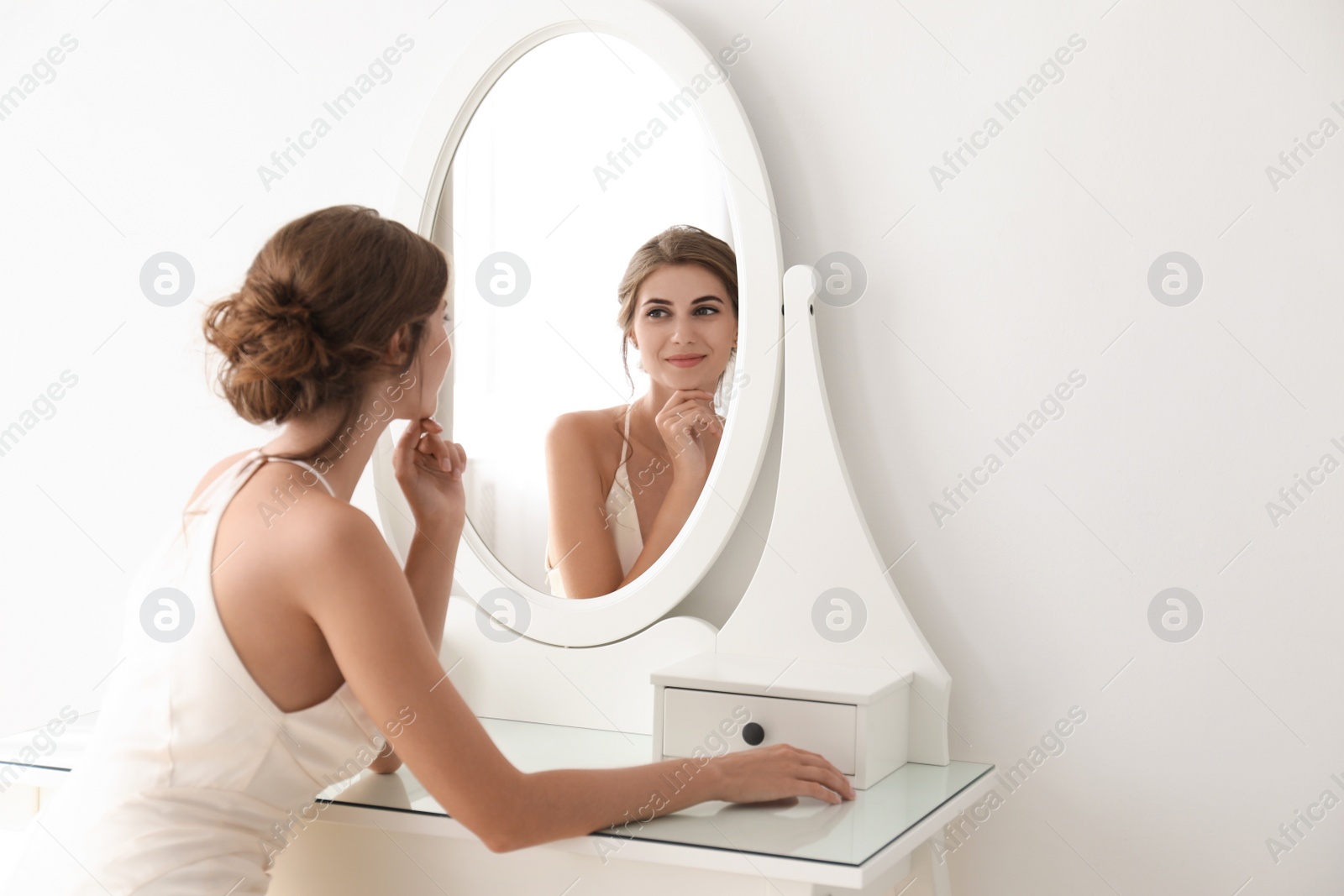 Photo of Young bride in beautiful wedding dress near mirror indoors