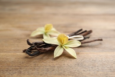 Photo of Aromatic vanilla sticks and flowers on wooden table, closeup