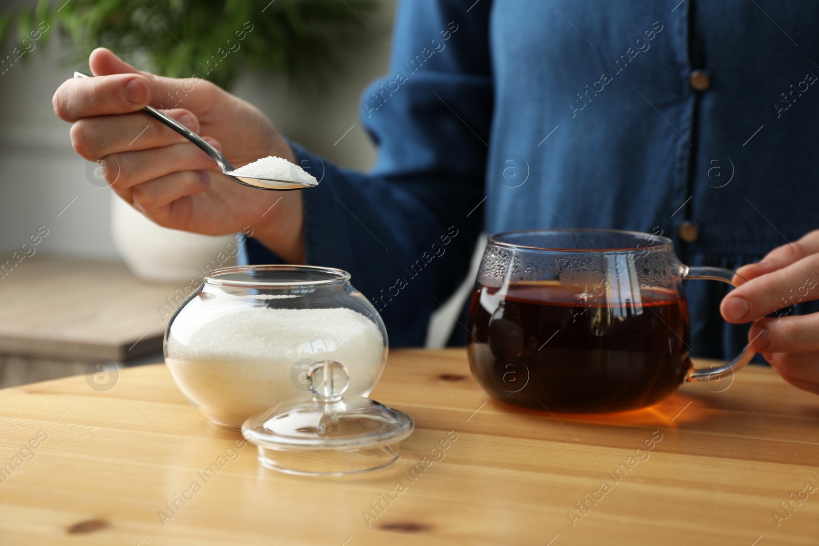 Photo of Woman adding sugar into aromatic tea at wooden table indoors, closeup