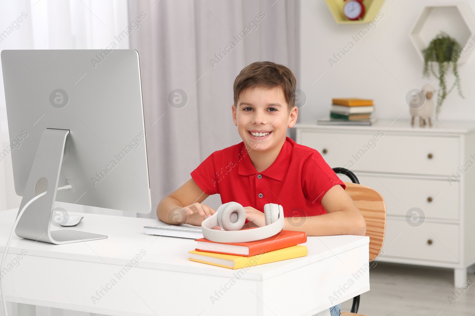 Photo of Boy using computer at desk in room. Home workplace