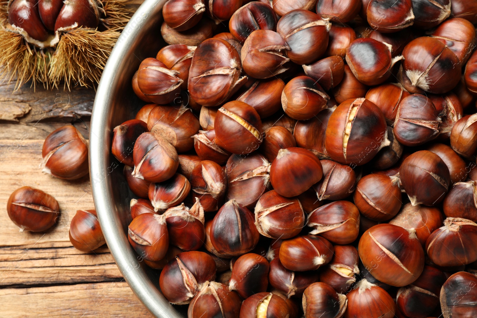 Photo of Delicious roasted edible chestnuts in bowl on wooden table, above view