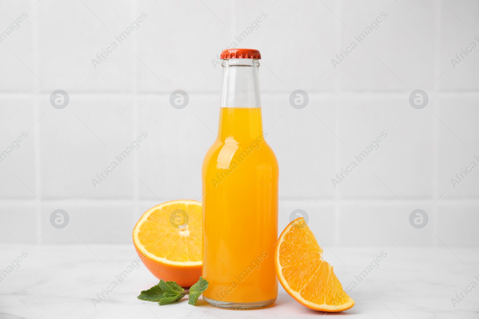 Photo of Delicious kombucha in glass bottle, orange and mint on white table