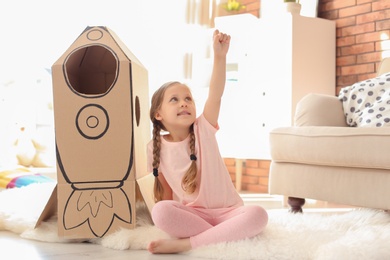 Adorable little child playing with cardboard rocket at home