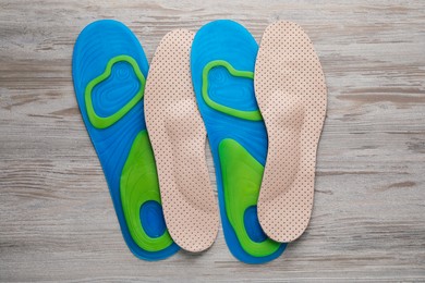 Photo of LIght blue and beige orthopedic insoles on wooden background, flat lay