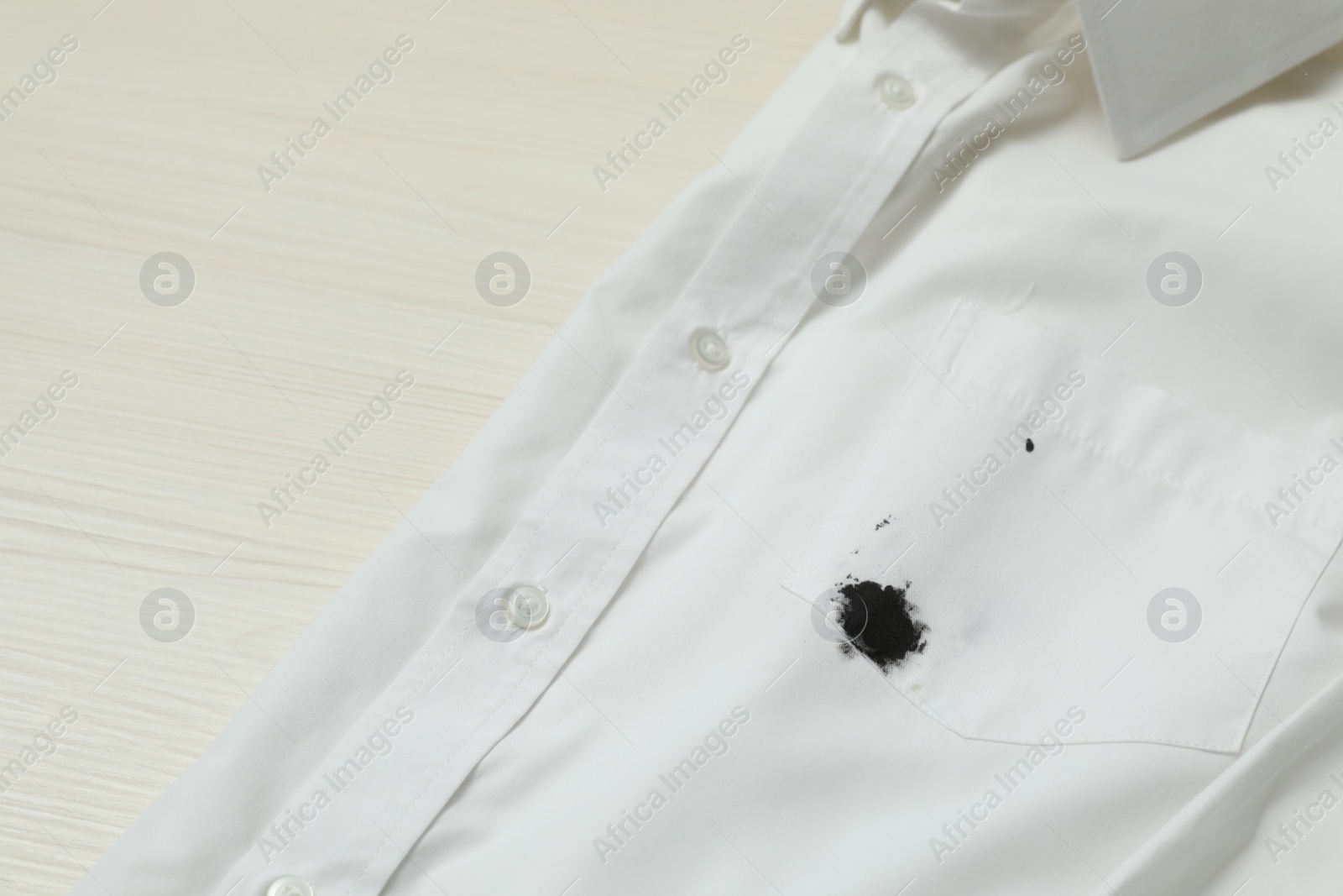 Photo of White shirt with stain of black ink on wooden table, closeup. Space for text