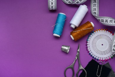 Photo of Flat lay composition with thimble and different sewing tools on purple background, space for text