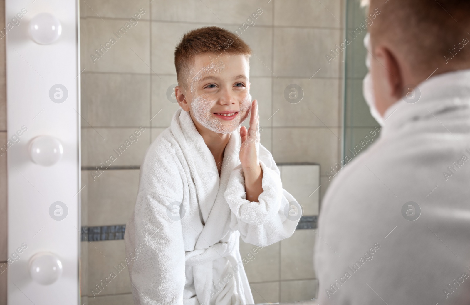 Photo of Little boy washing face with soap near mirror in bathroom