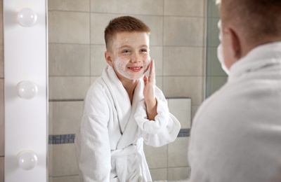 Photo of Little boy washing face with soap near mirror in bathroom