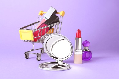 Stylish pocket mirror and makeup products on lilac background