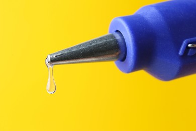 Photo of Dripping hot glue from gun on yellow background, closeup