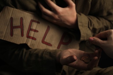 Photo of Woman giving coins to homeless with help sign, closeup. Charity and donation