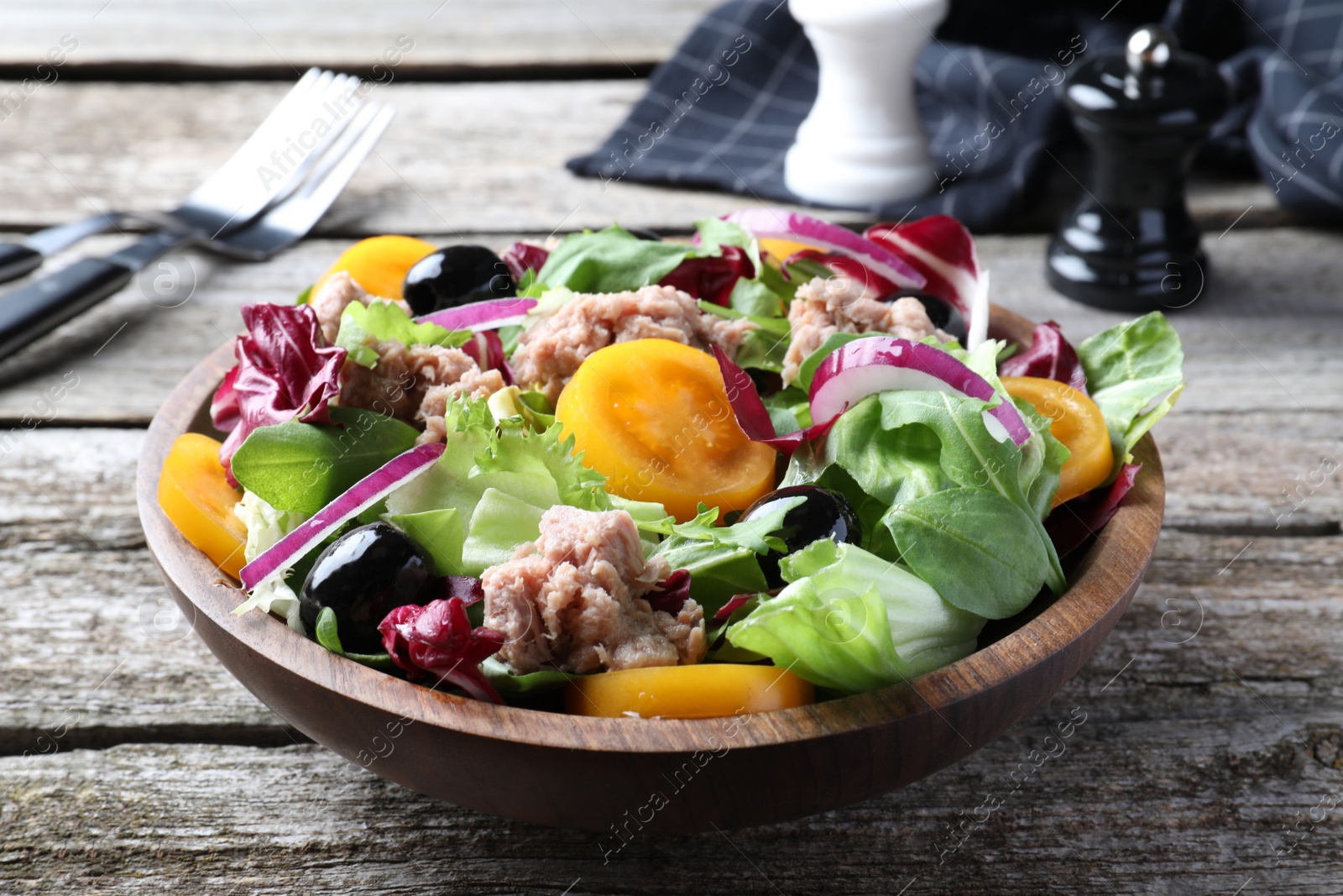 Photo of Bowl of delicious salad with canned tuna and vegetables on wooden table