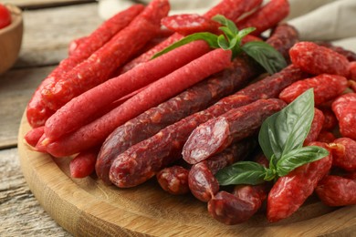 Photo of Different thin dry smoked sausages and basil on wooden table, closeup