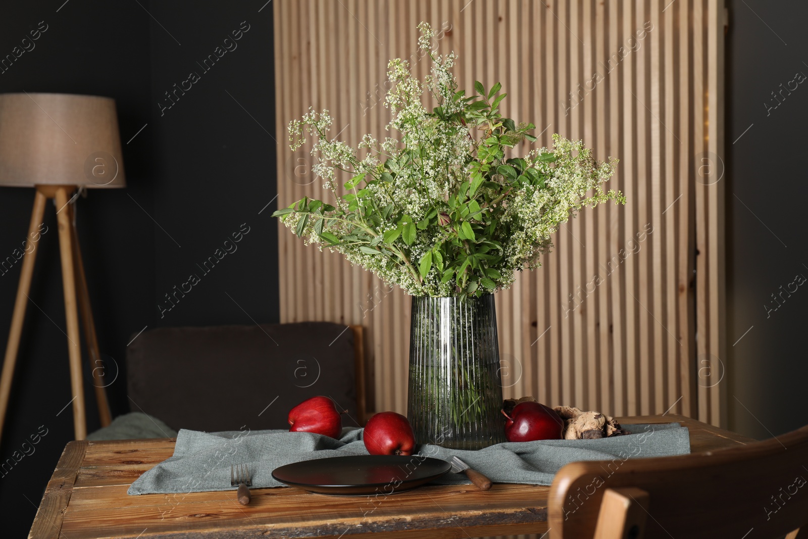 Photo of Set of clean dishware, ripe red apples and flowers on wooden table in stylish dining room