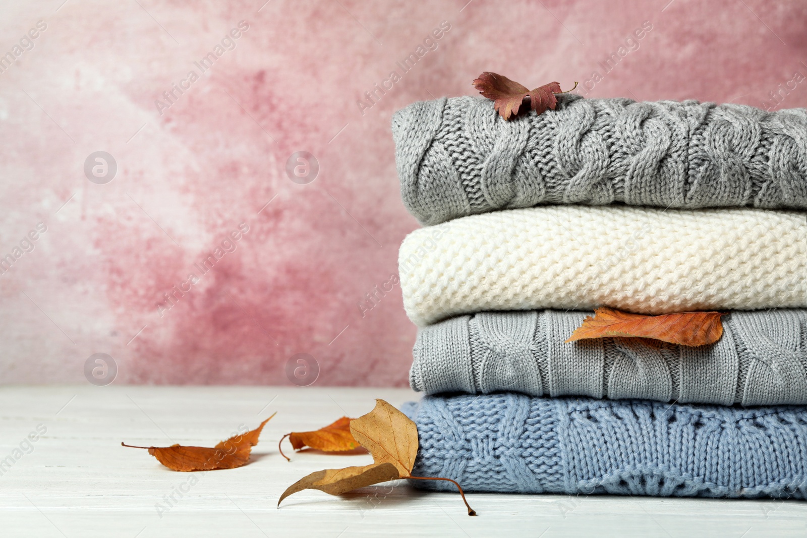 Photo of Stack of warm clothes and autumn leaves on white wooden table against light background. Space for text