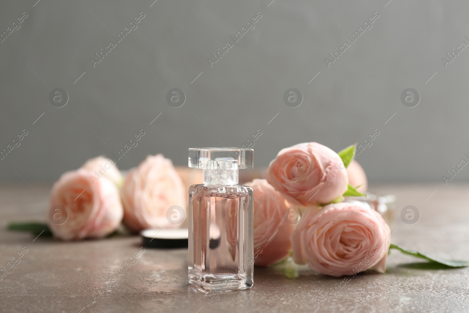 Photo of Bottle of perfume and roses on table against grey background