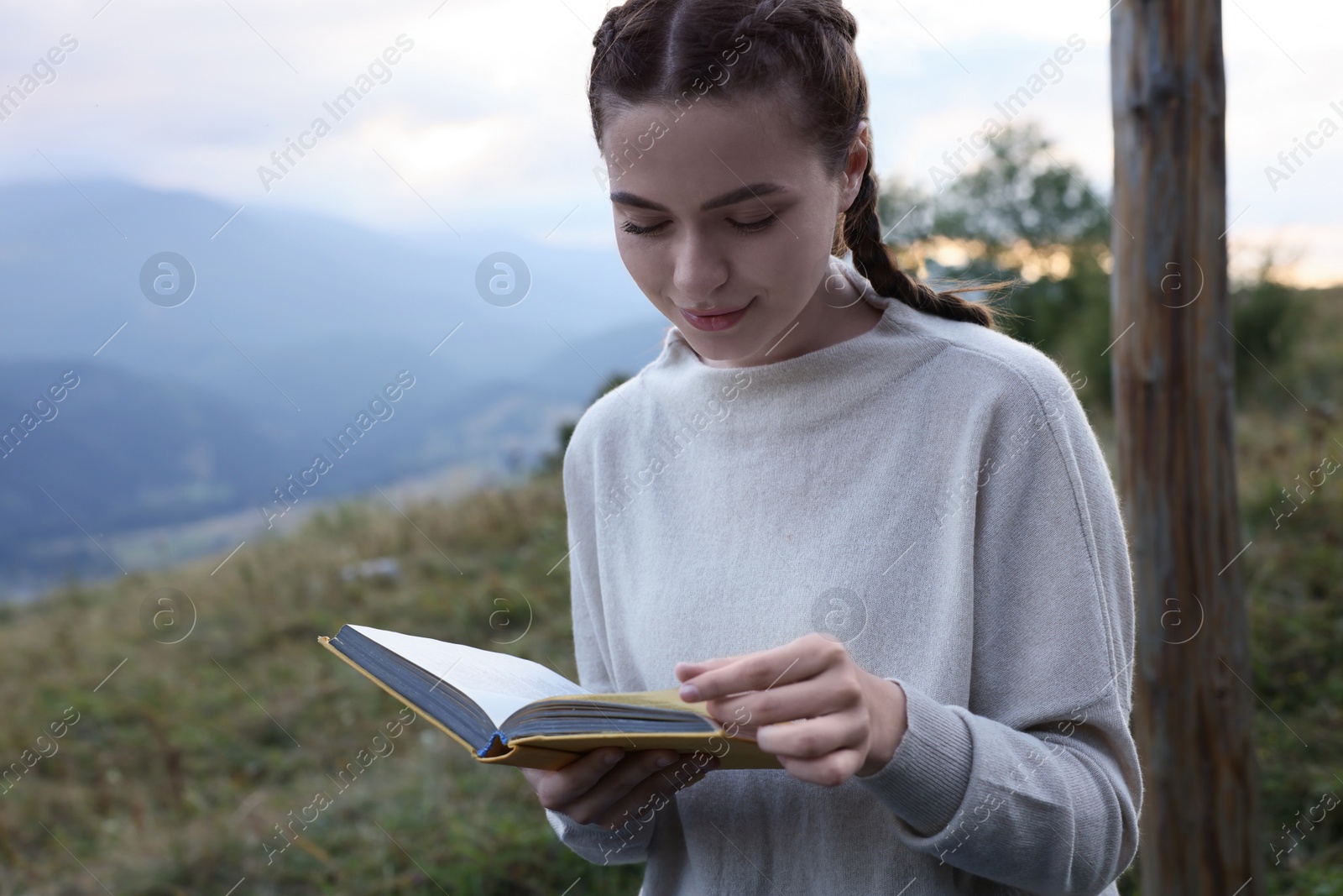 Photo of Beautiful young woman reading book in mountains, space for text