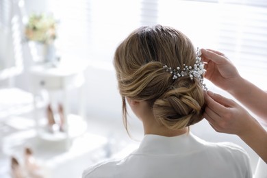 Professional stylist making wedding hairstyle for bride in salon, back view