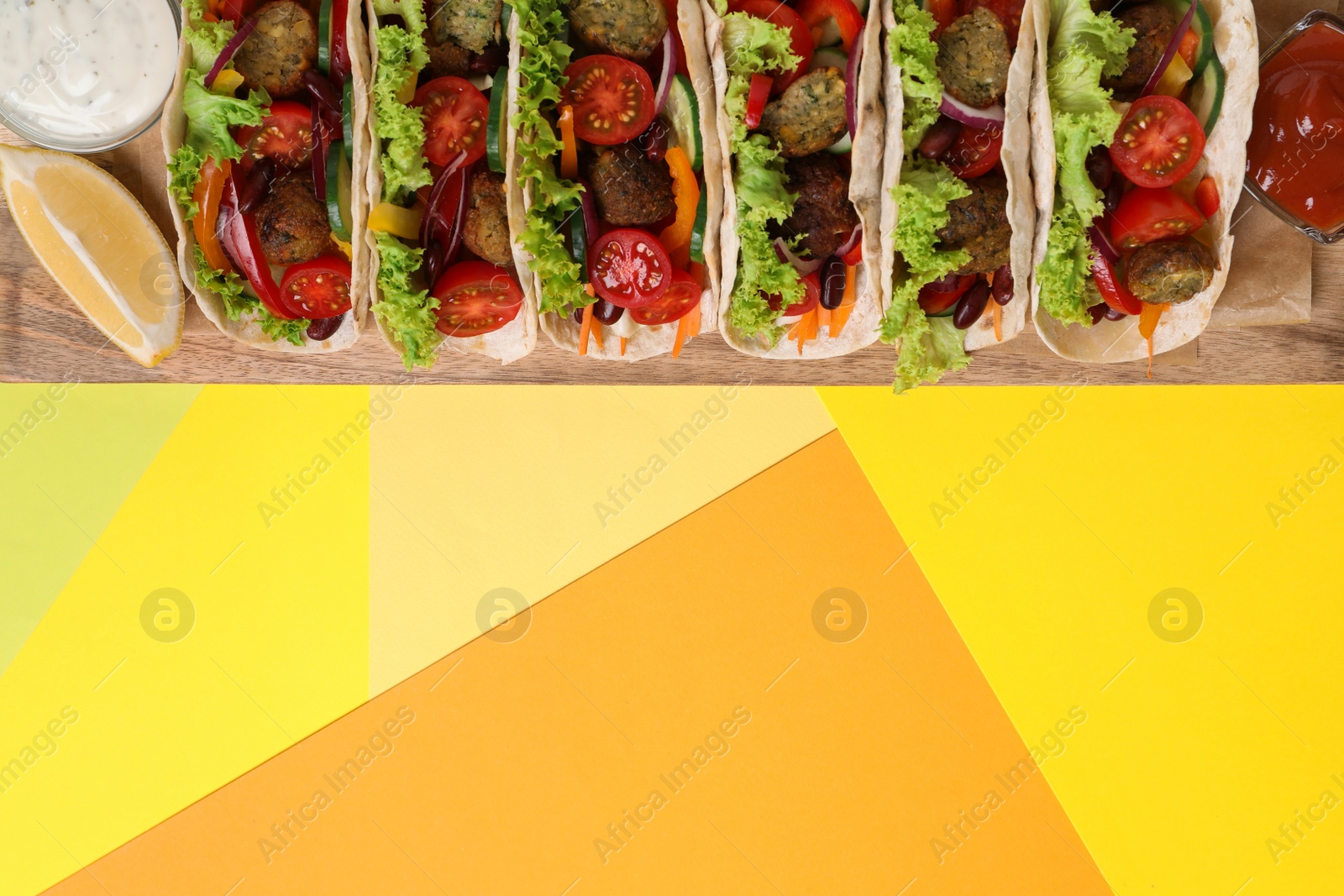 Photo of Many delicious vegetarian tacos served on yellow table, top view. Space for text