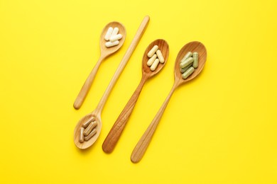 Photo of Different vitamin pills in spoons on yellow background, flat lay